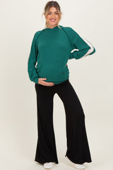 woman wearing a green ribbed maternity top with white stripes and black wide-leg maternity pants, showing her baby bump