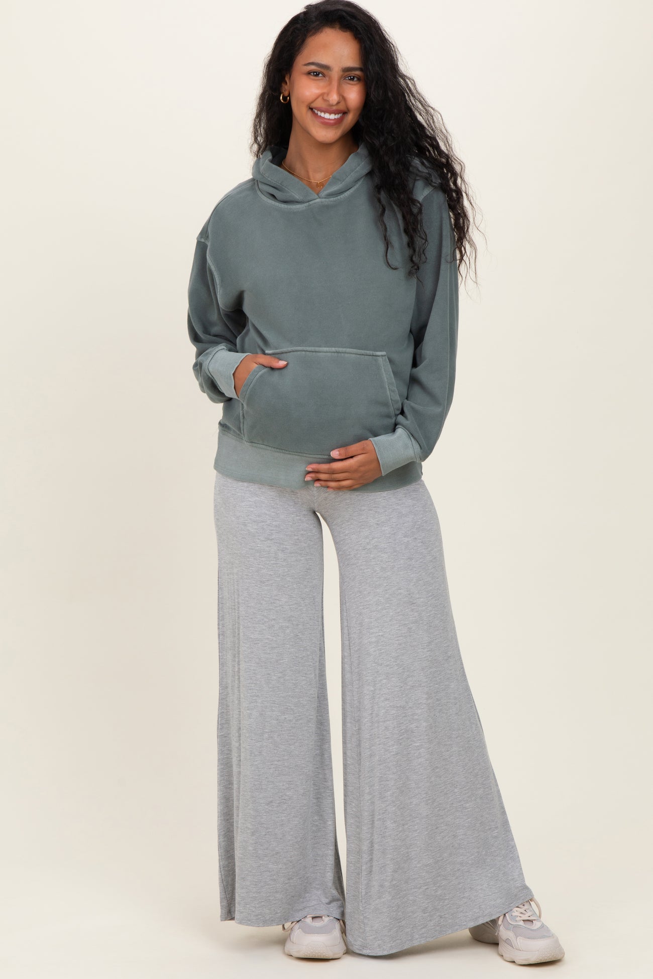 woman wearing a green maternity hoodie and gray wide-leg sweatpants, holding her baby bump
