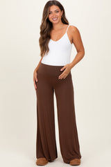 woman wearing a white maternity bodysuit and brown wide-leg maternity pants, showing her baby bump
