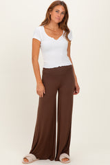 woman wearing a white ribbed short sleeve top and brown wide-leg pants, standing with one hand on her hip
