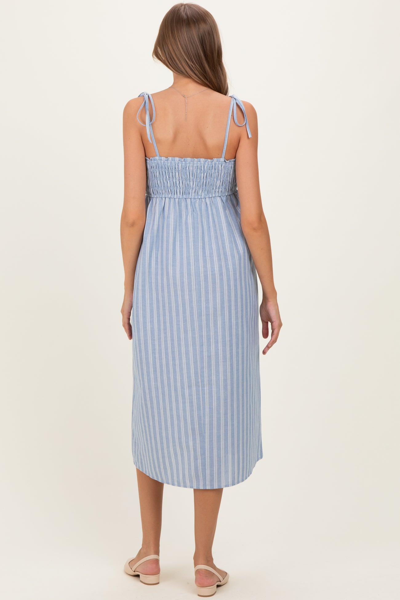 woman wearing a blue and white striped maternity dress with adjustable tie straps and a smocked back