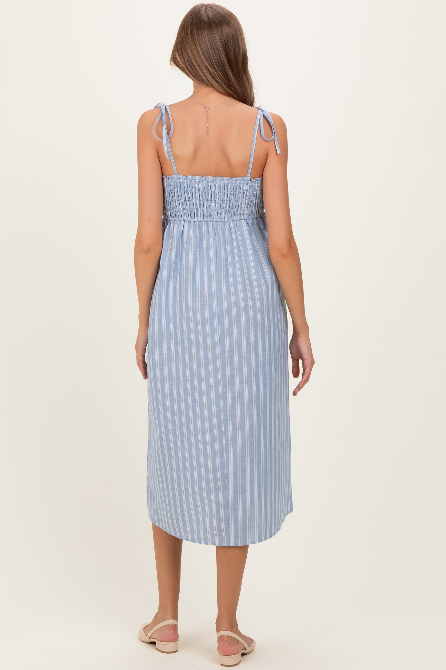 woman wearing a blue and white striped maternity dress with adjustable tie straps and a smocked back
