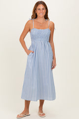 woman wearing a light blue striped maxi dress with smocked bodice and adjustable straps, posing with pockets