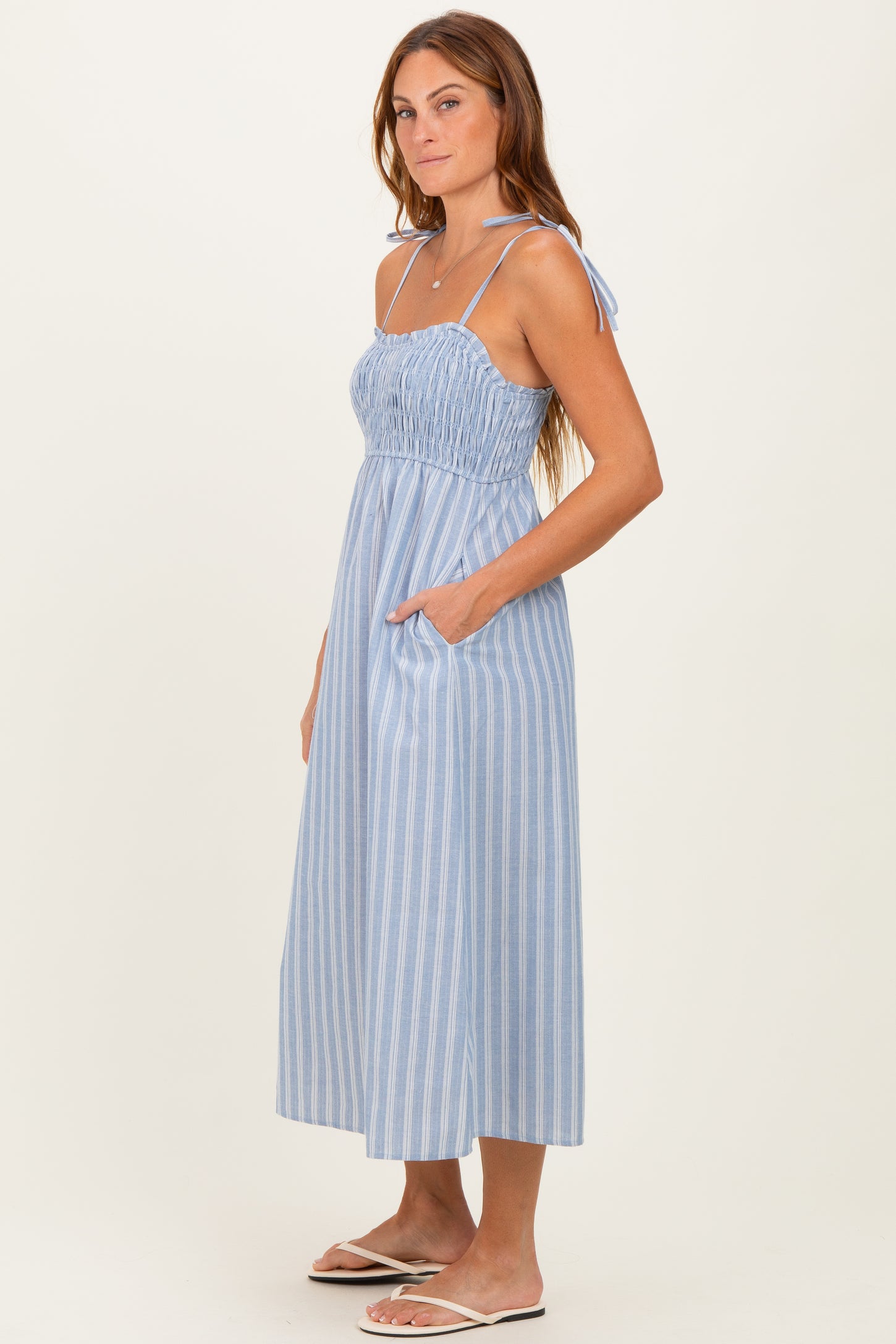 woman wearing a blue and white striped midi dress with a smocked bodice and tie straps, featuring side pockets