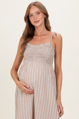 woman wearing a beige and white striped maternity dress with smocked bodice and holding her baby bump