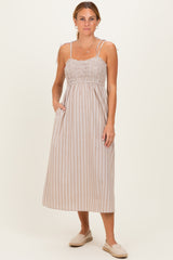 woman wearing a brown and beige striped maxi dress with smocked bodice and tie straps, standing with hands in pockets