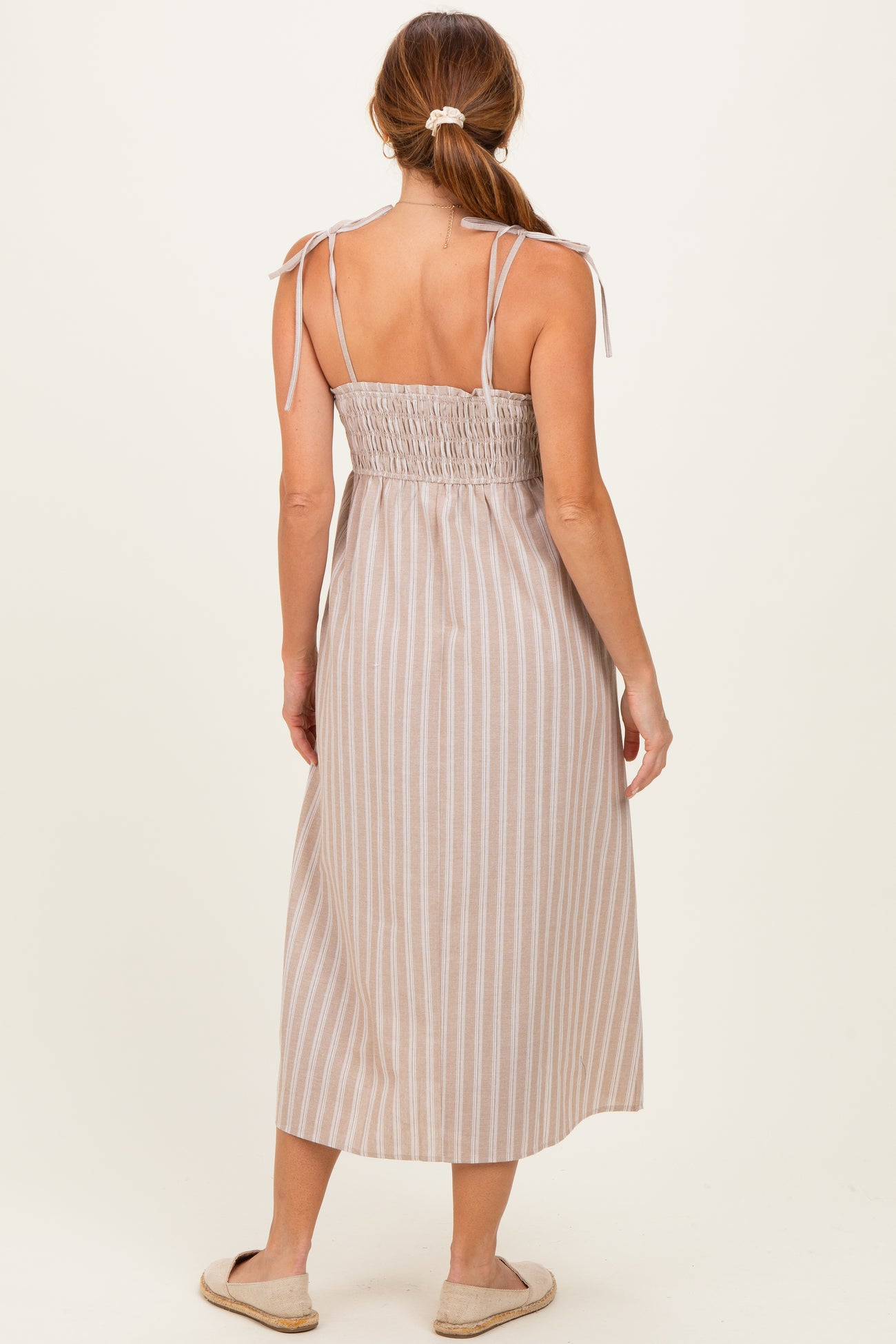 woman wearing a tan and white striped smocked back maxi dress with adjustable tie straps and a flowy silhouette