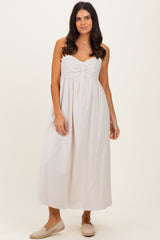 woman wearing a light beige sleeveless maxi dress with a ruched bodice and a flowy skirt