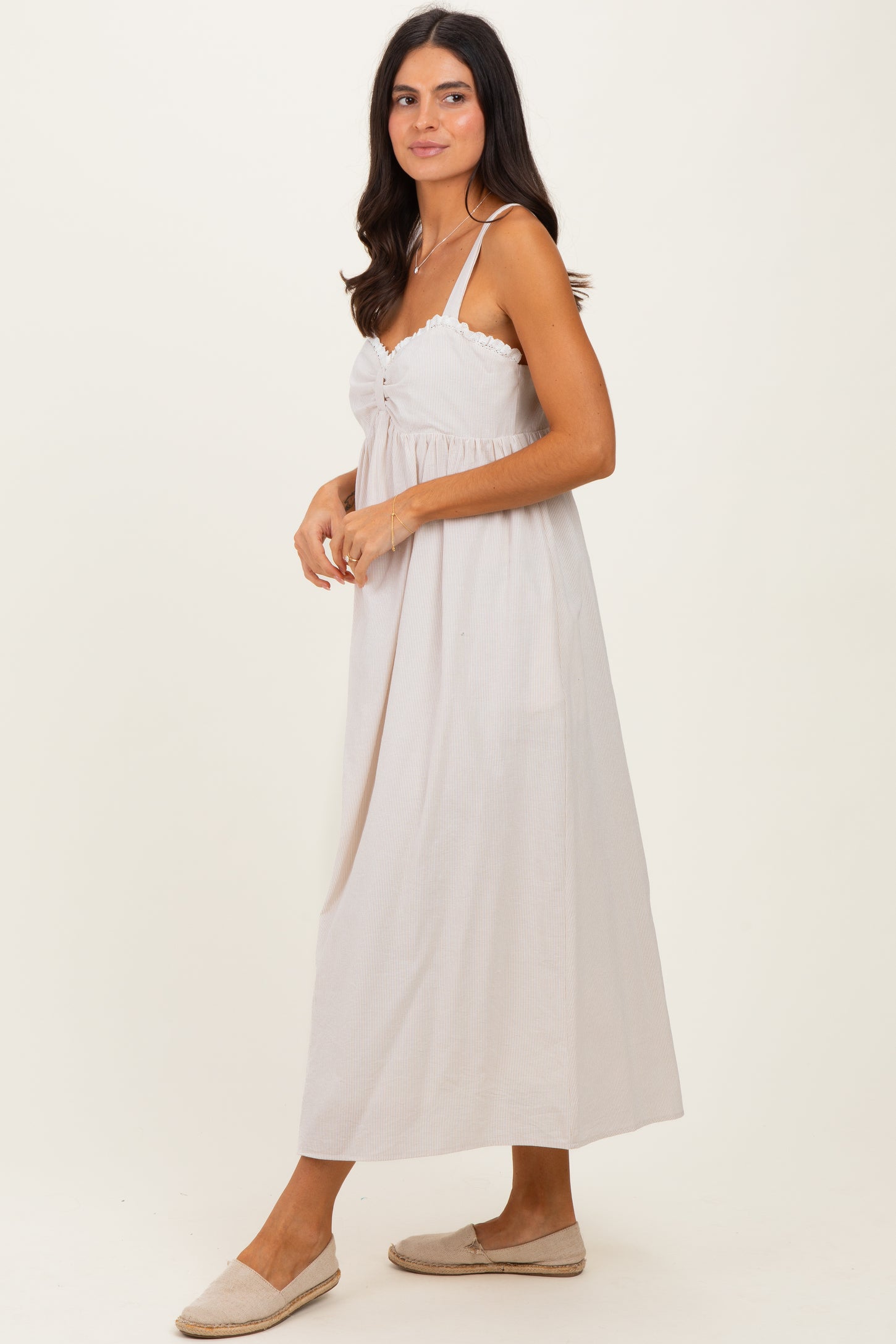 woman wearing a light beige striped maxi dress with adjustable straps and a gathered front detail