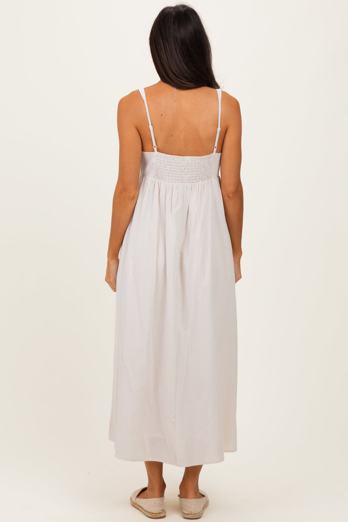 woman wearing a light beige striped maxi dress with a smocked back and spaghetti straps, viewed from the back
