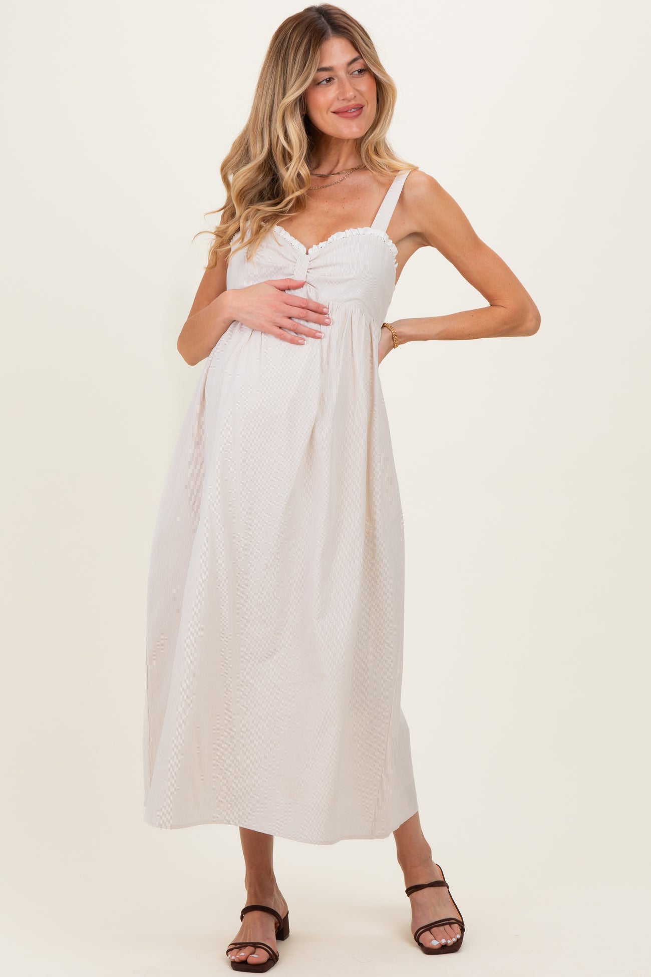 woman wearing a light pink maternity maxi dress with a button detail and holding her baby bump