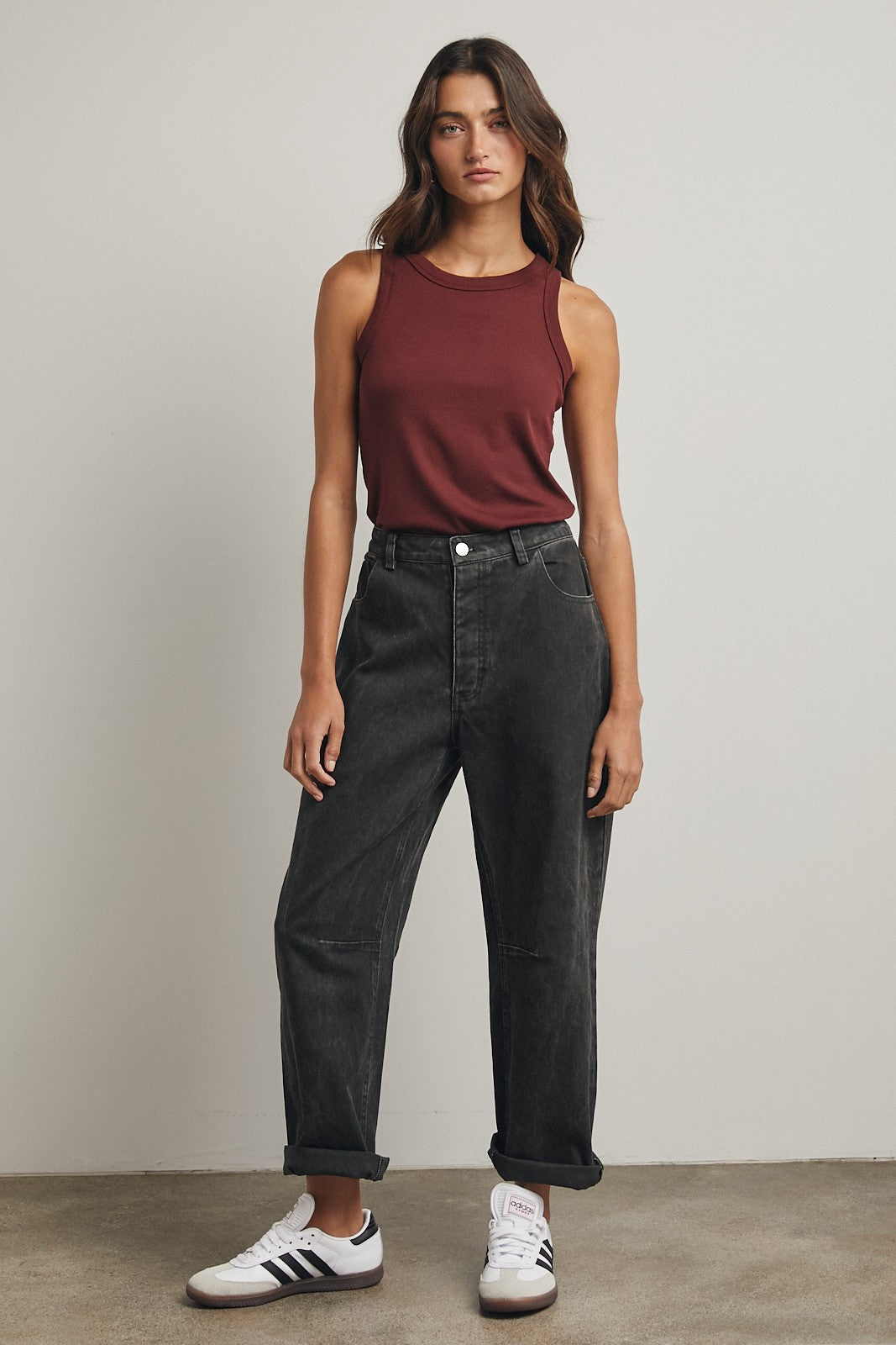 woman wearing a maroon sleeveless top and high-waisted black jeans, styled with rolled cuffs and white sneakers