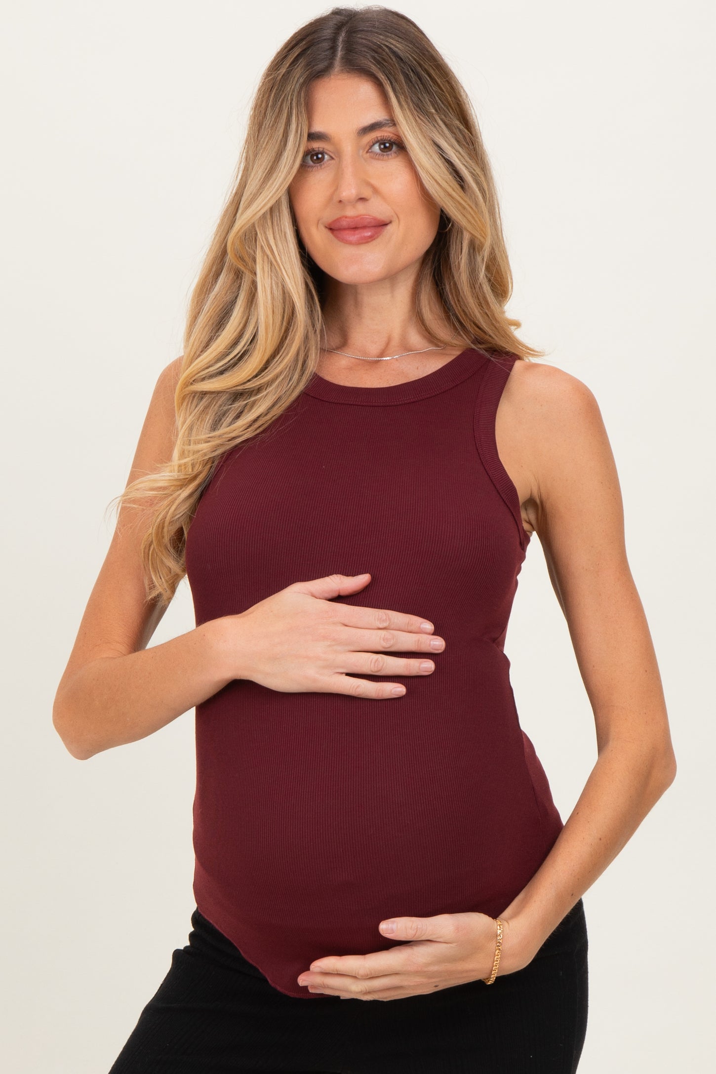 woman wearing a burgundy ribbed maternity tank top and holding her baby bump