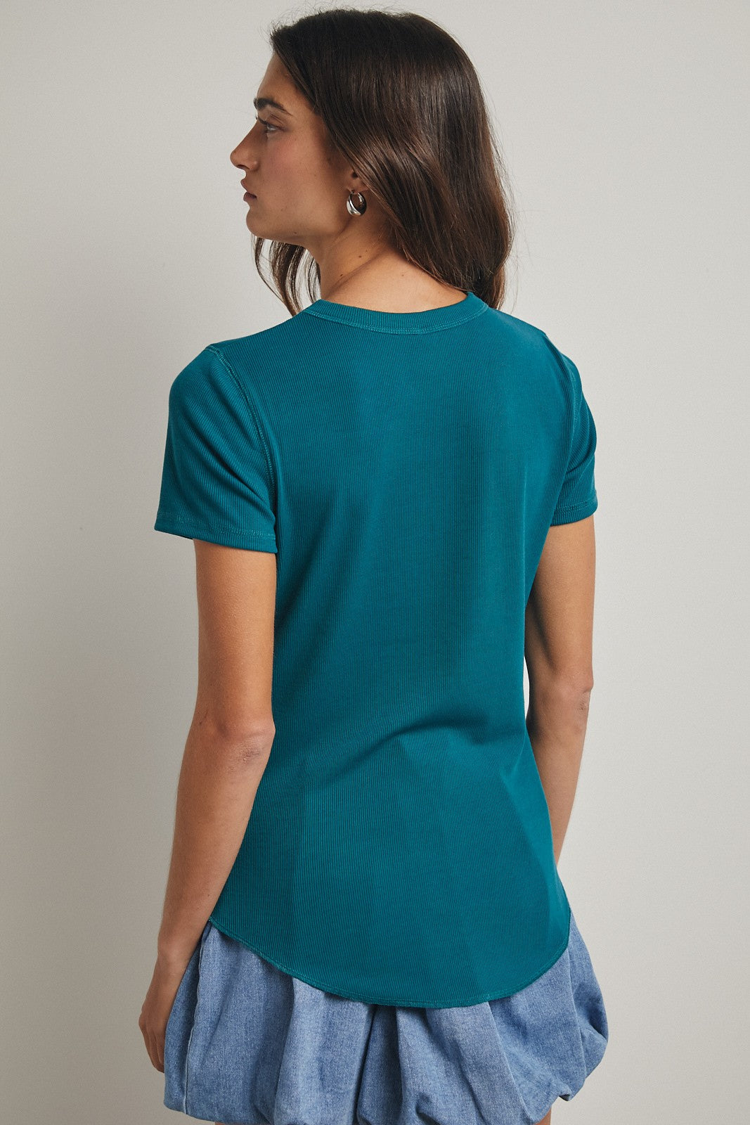 woman wearing a teal short sleeve top with a rounded hem and a relaxed fit, showing the back view