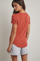 woman wearing a rust red short sleeve top paired with gray ruffled hem shorts, viewed from the back