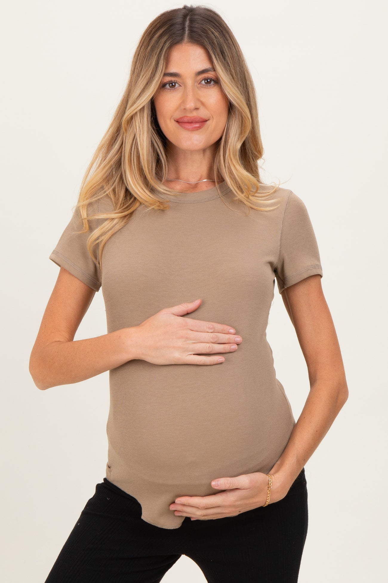 woman wearing a beige ribbed maternity top and holding her baby bump