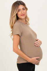 woman wearing a light brown ribbed maternity top and gently holding her pregnant belly