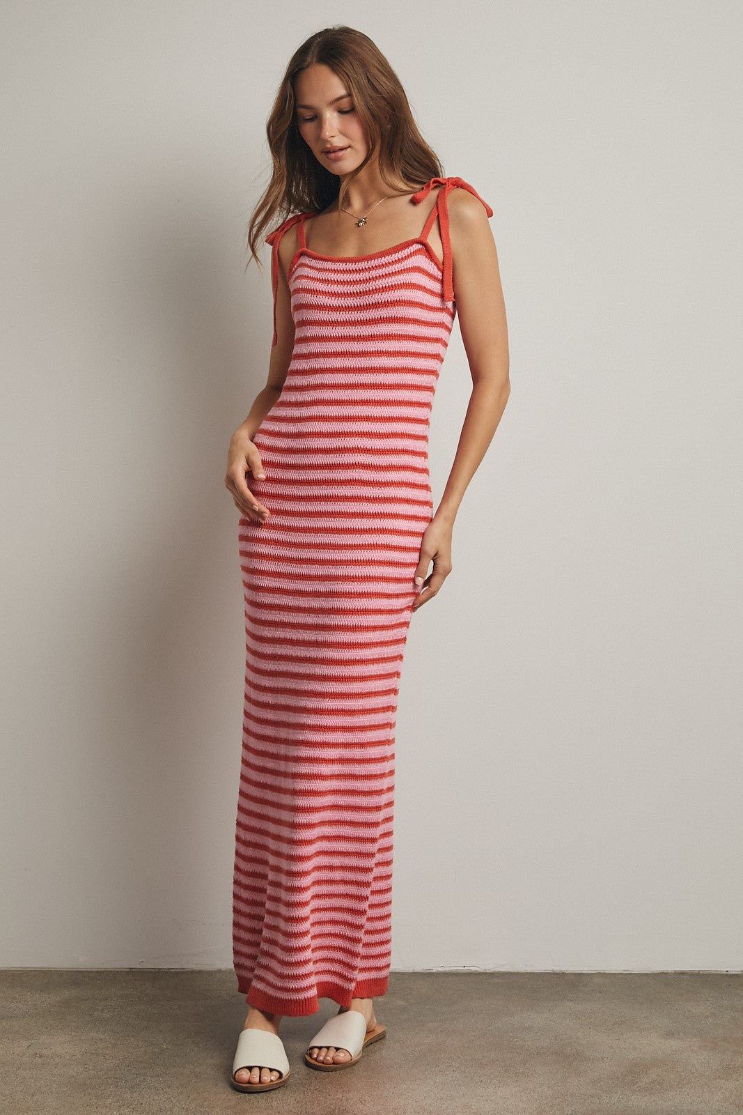 woman wearing a red and pink striped maxi dress with adjustable tie straps and a fitted silhouette