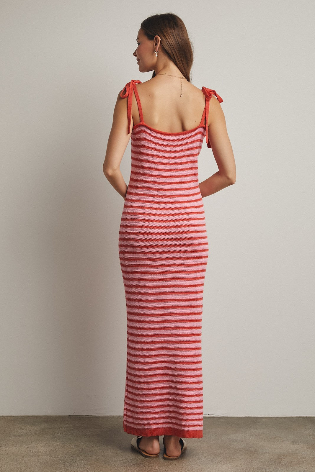 woman wearing a pink and red striped spaghetti strap maxi dress with tie details on the shoulders