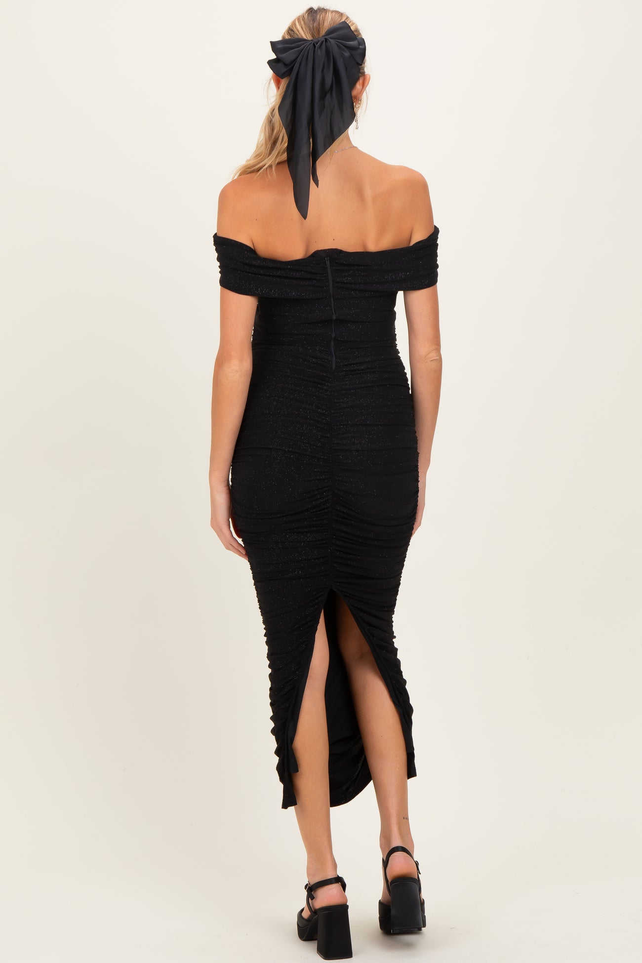 woman wearing a black off-shoulder maternity dress with ruched detailing and a side slit, showing a baby bump
