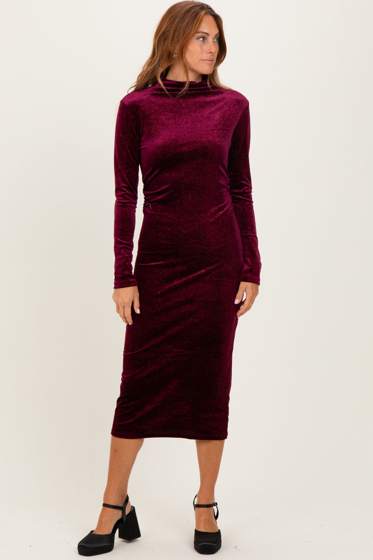 woman wearing a burgundy long sleeve velvet midi dress with a mock neck and fitted silhouette