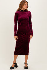 woman wearing a burgundy long sleeve velvet midi dress with a mock neck and fitted silhouette