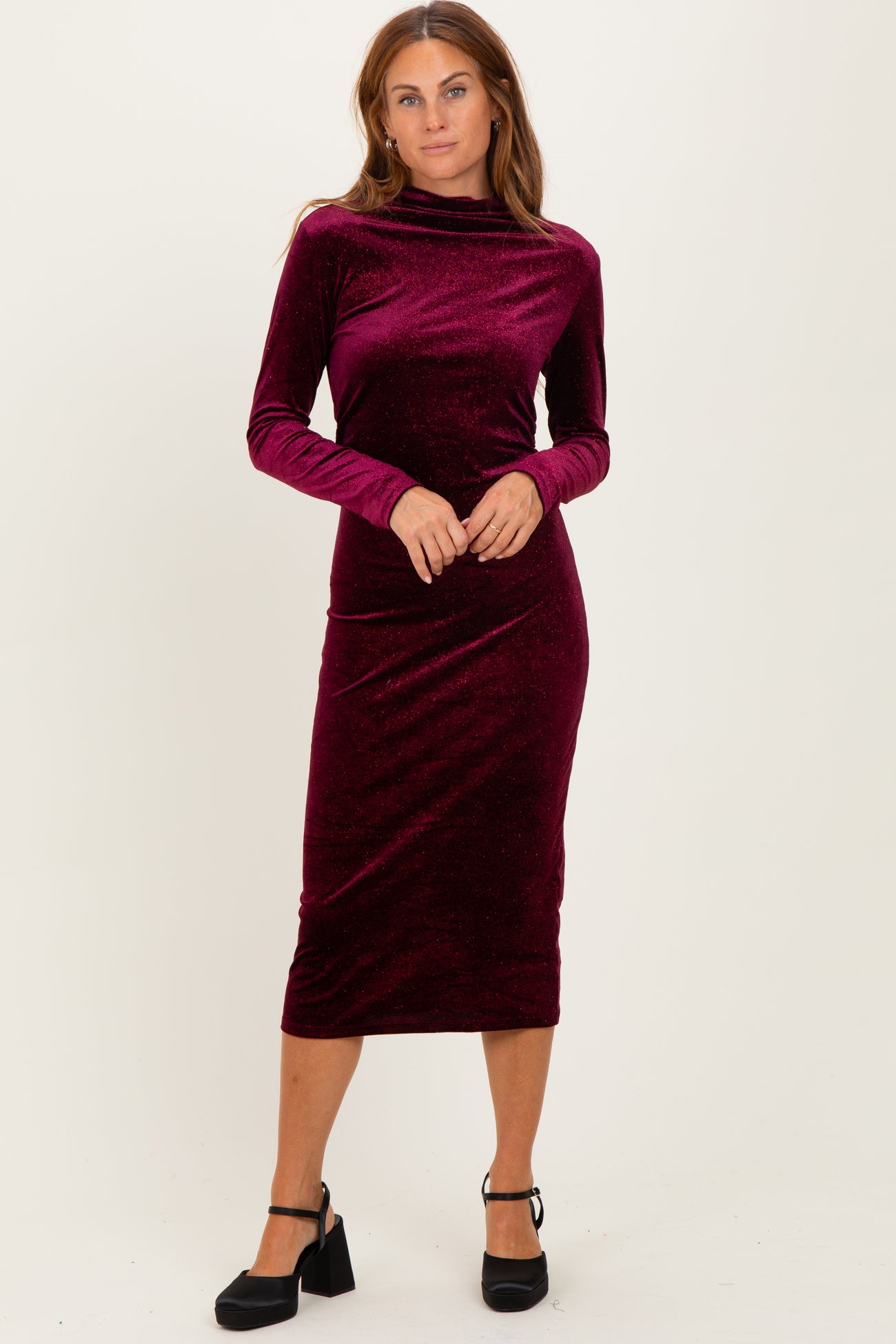 woman wearing a burgundy long sleeve velvet midi dress with a high neck and a fitted silhouette