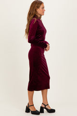 woman wearing a burgundy velvet long sleeve midi dress with a fitted silhouette and block heel shoes