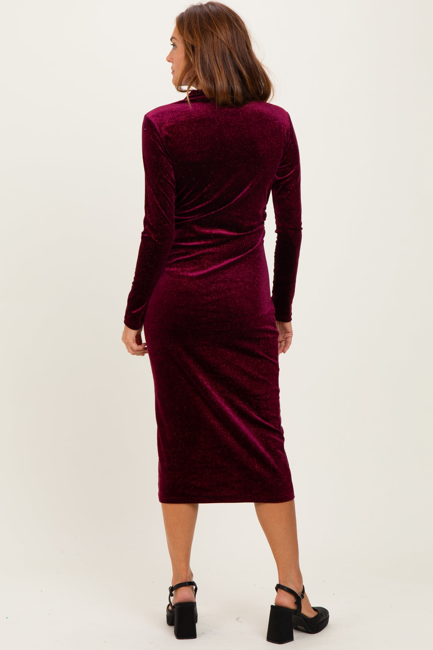 woman wearing a burgundy velvet long sleeve midi dress, viewed from the back, with fitted silhouette and below-the-knee length