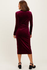 woman wearing a burgundy velvet long sleeve midi dress, viewed from the back, with fitted silhouette and below-the-knee length