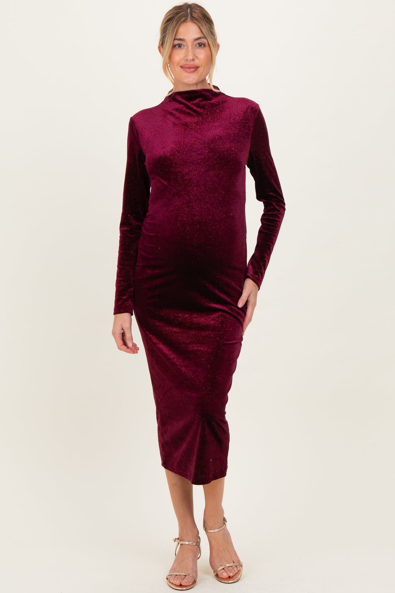 woman wearing a burgundy long sleeve maternity dress with a fitted silhouette and high neckline, showing her baby bump