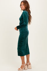 woman wearing a teal velvet long sleeve midi dress with a fitted silhouette and side slit, standing sideways