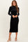 woman wearing a black long sleeve velvet midi dress with a high neck and fitted silhouette, standing in heels