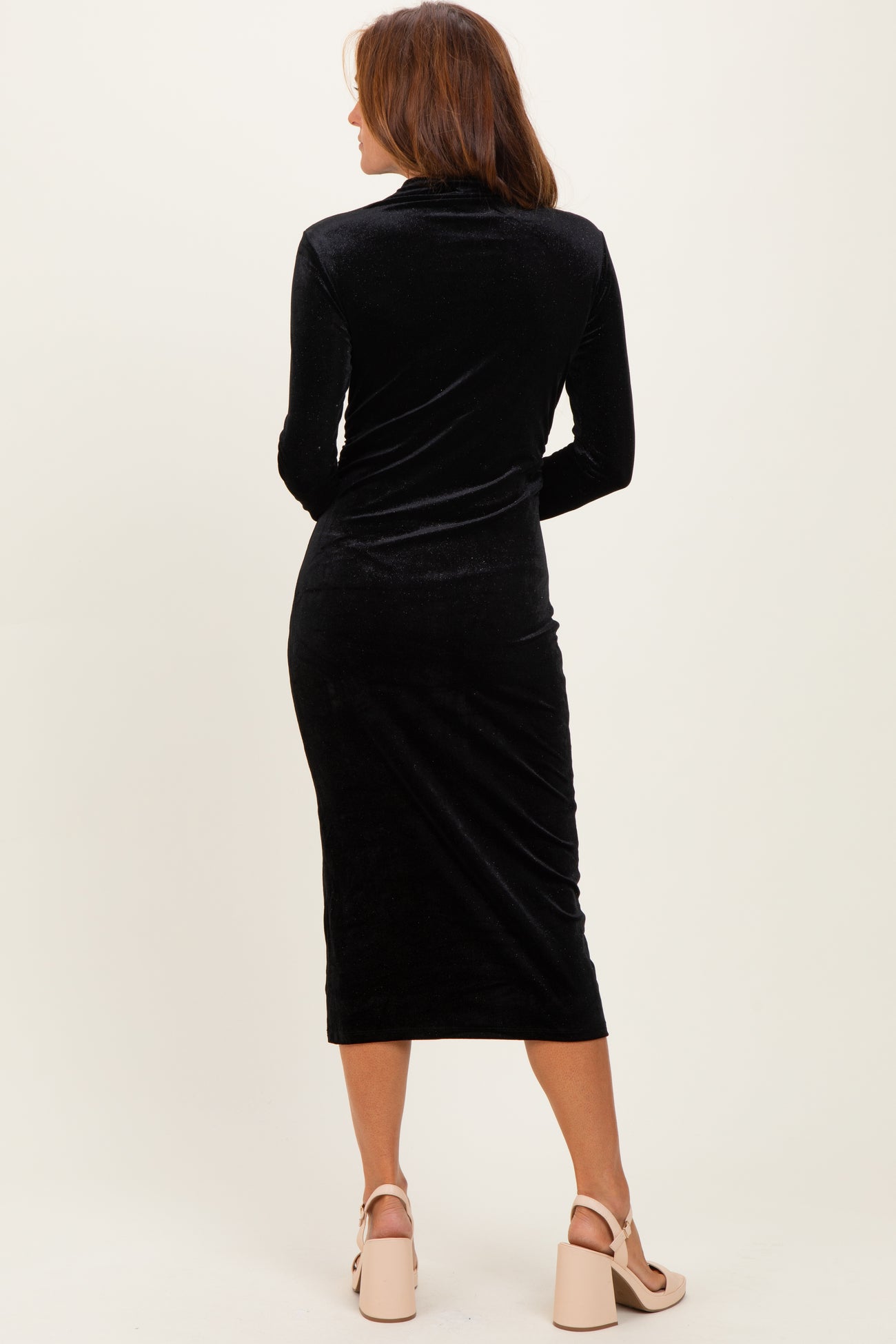 woman wearing a black velvet long sleeve midi dress with a fitted silhouette and a high neck