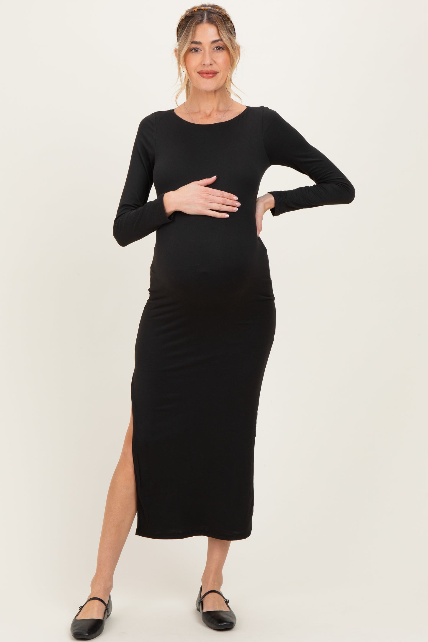 woman wearing a black long sleeve maternity dress with a side slit and holding her baby bump