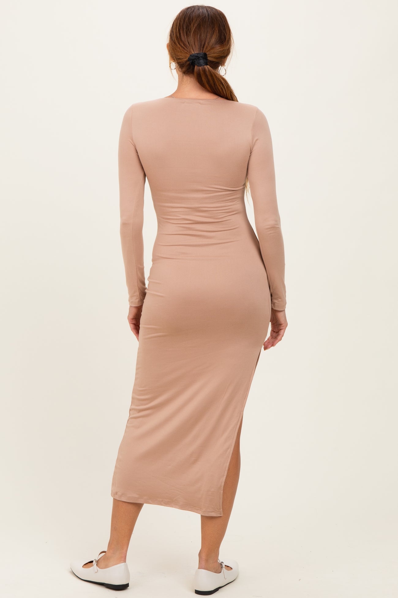 woman wearing a fitted long sleeve beige midi dress with side slits shown from the back