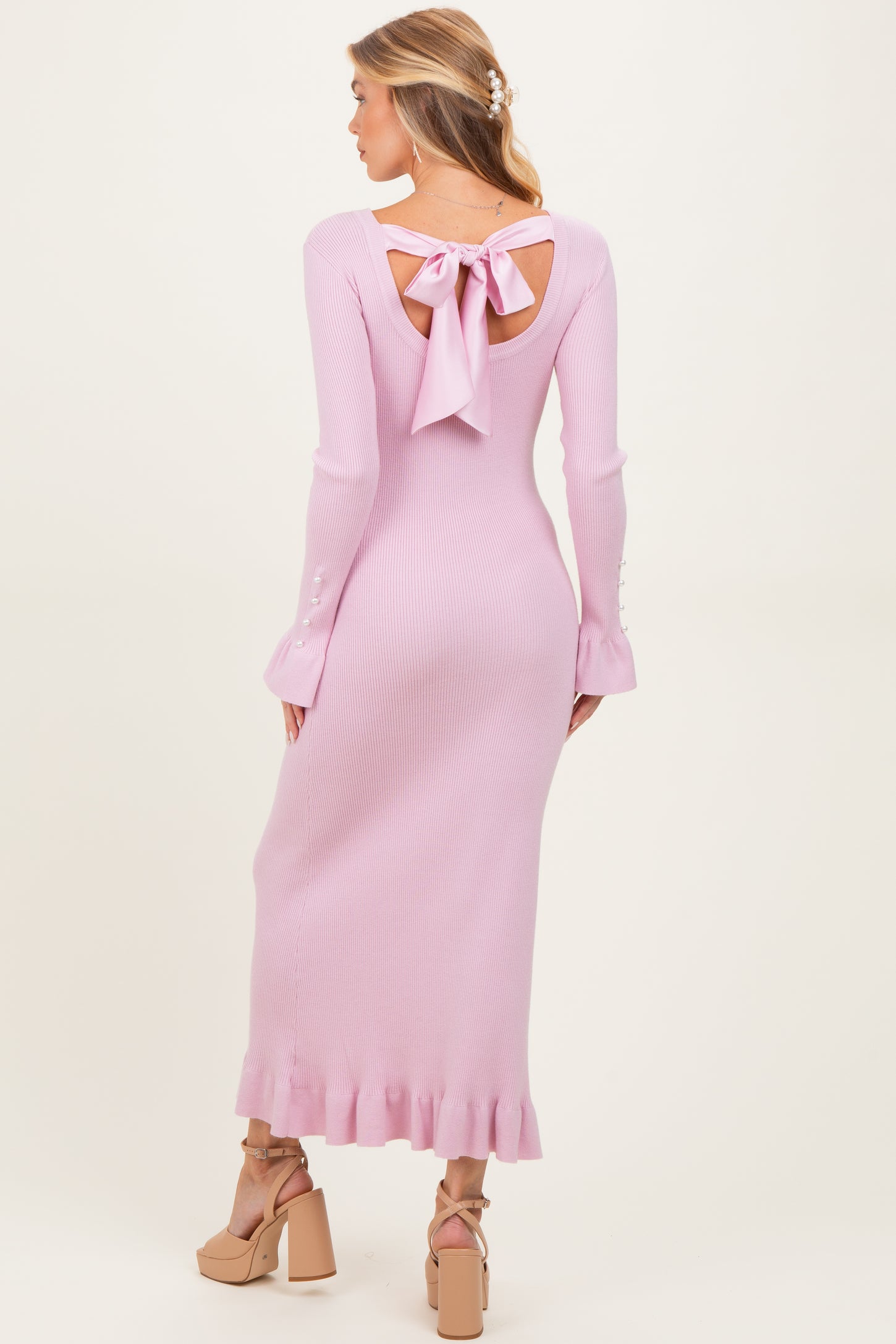 maternity wear in pink ribbed knit with a bow detail at the back and flared sleeves, model showing off a baby bump