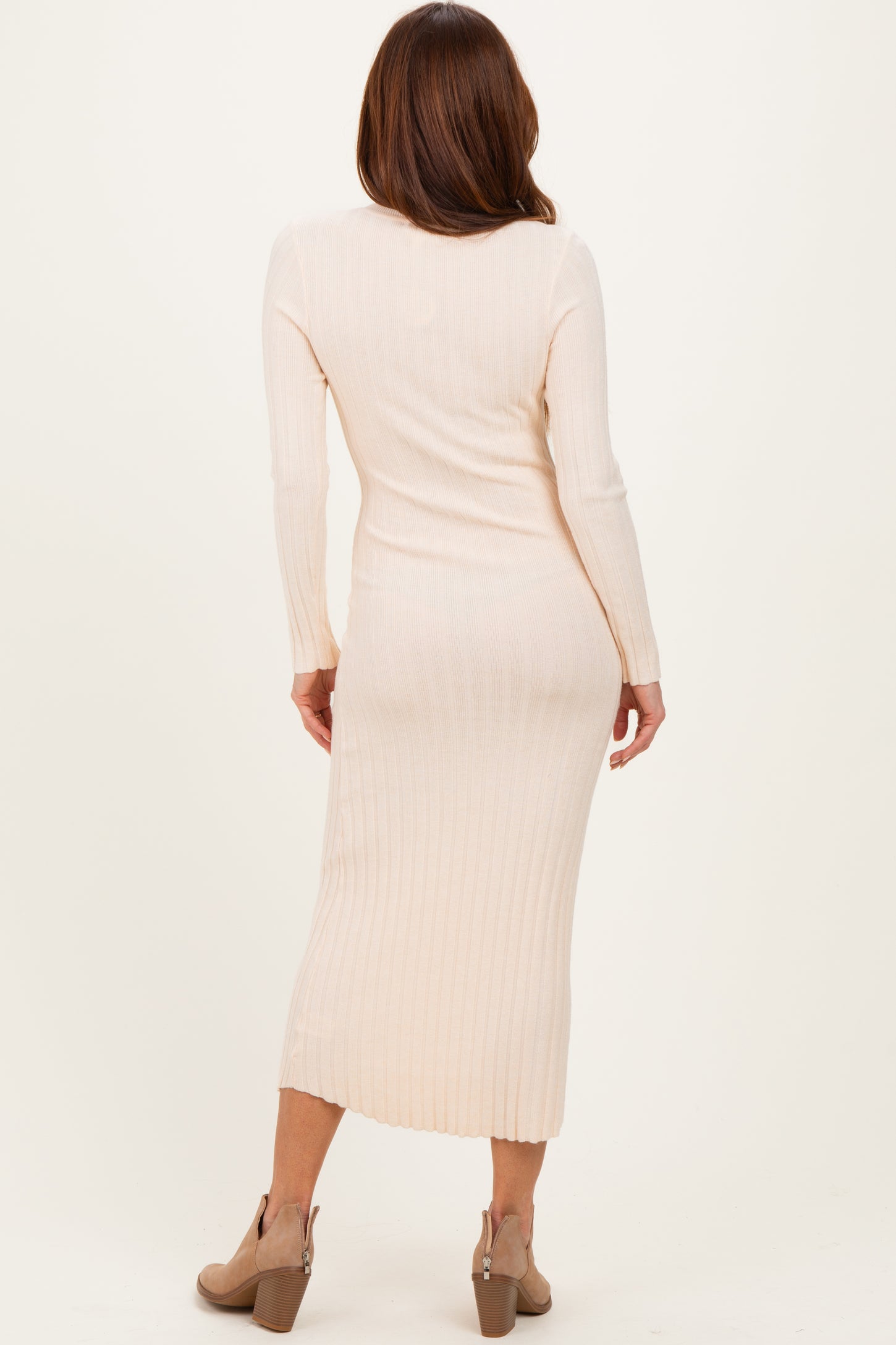 woman wearing a fitted light beige ribbed midi dress with long sleeves and a side slit, seen from the back