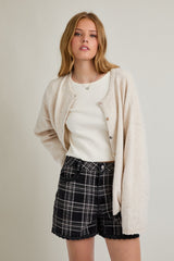 woman wearing a soft beige cardigan over a white tank top, paired with black and gray plaid shorts