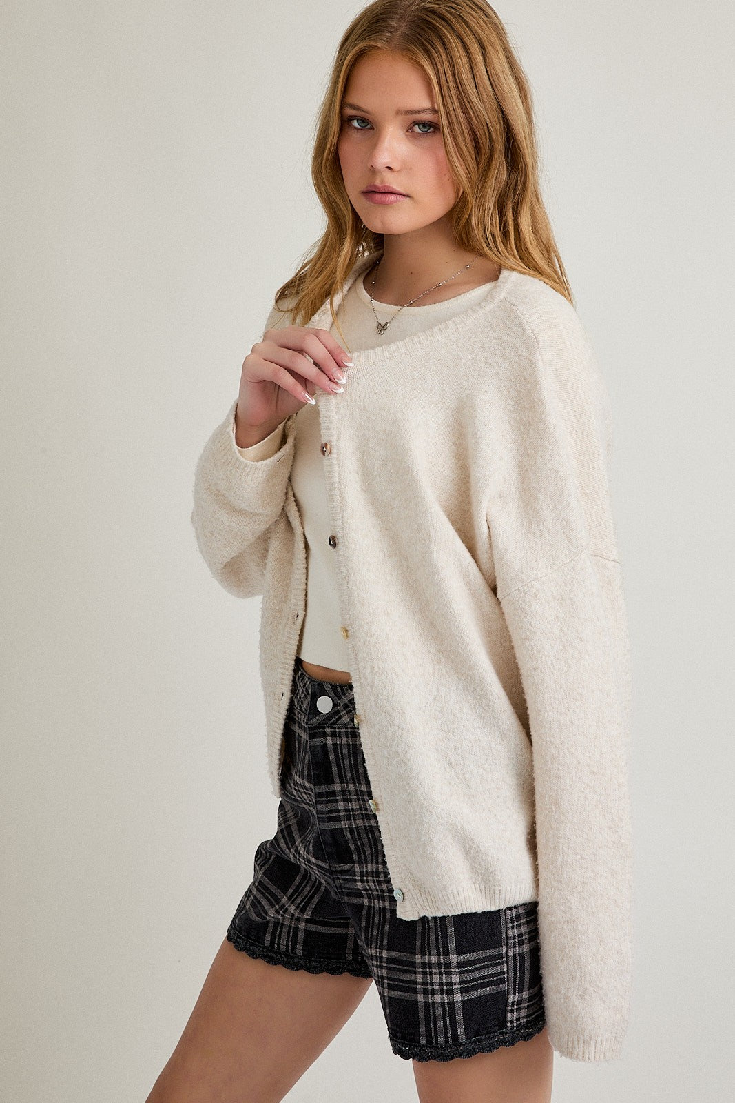 woman wearing a cream oversized cardigan over a white crop top paired with plaid shorts