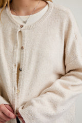 woman wearing a beige button-up cardigan over a light cream top, with a delicate necklace visible