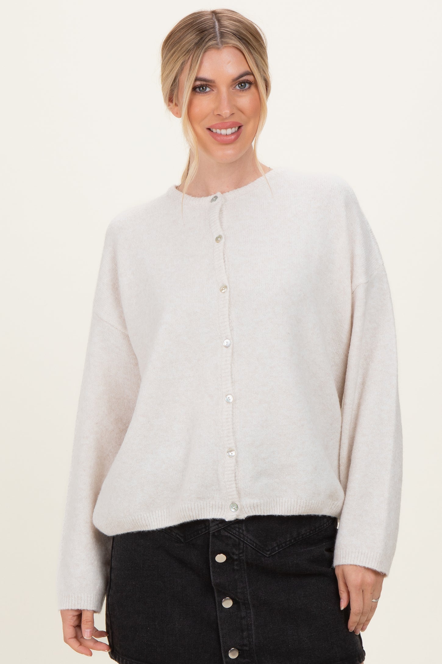 woman wearing a light beige oversized cardigan with pearl buttons and black denim skirt