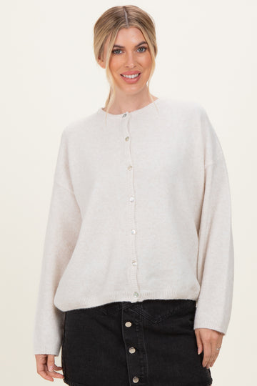 woman wearing a light beige oversized cardigan with pearl buttons and black denim skirt