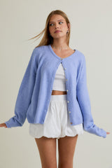 woman wearing a light blue oversized cardigan over a white cropped tank top and white skirt