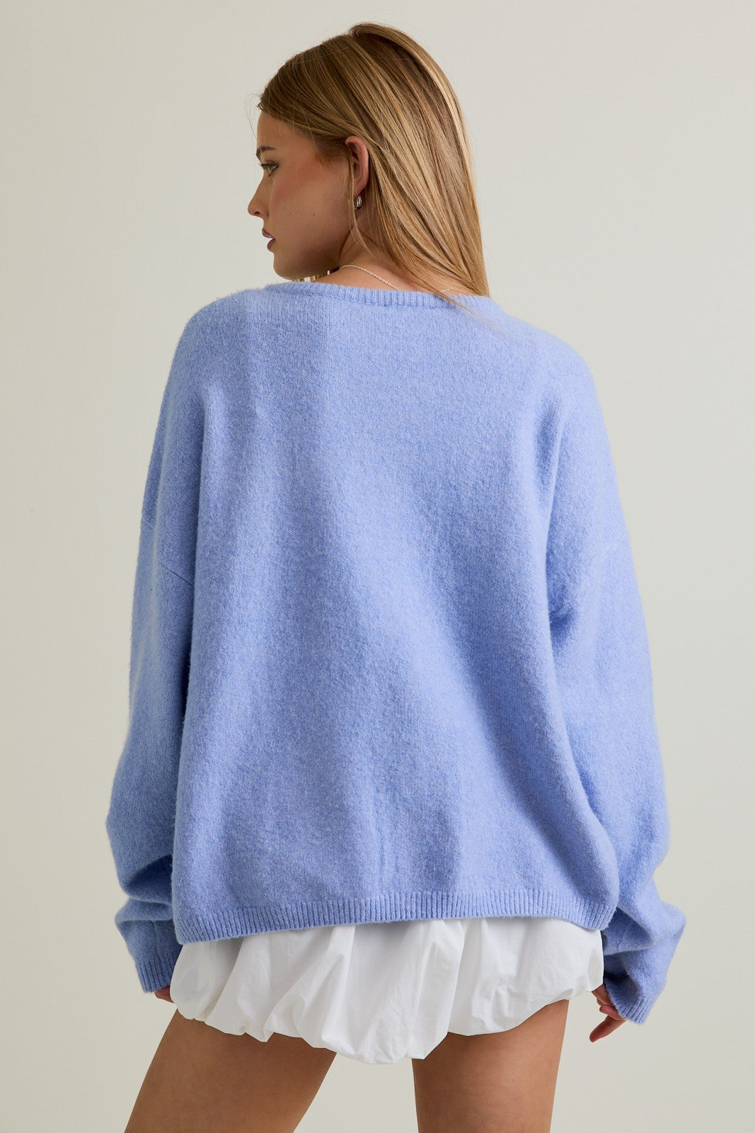 woman wearing a oversized light blue knit sweater with dropped shoulders and a white skirt, seen from the back