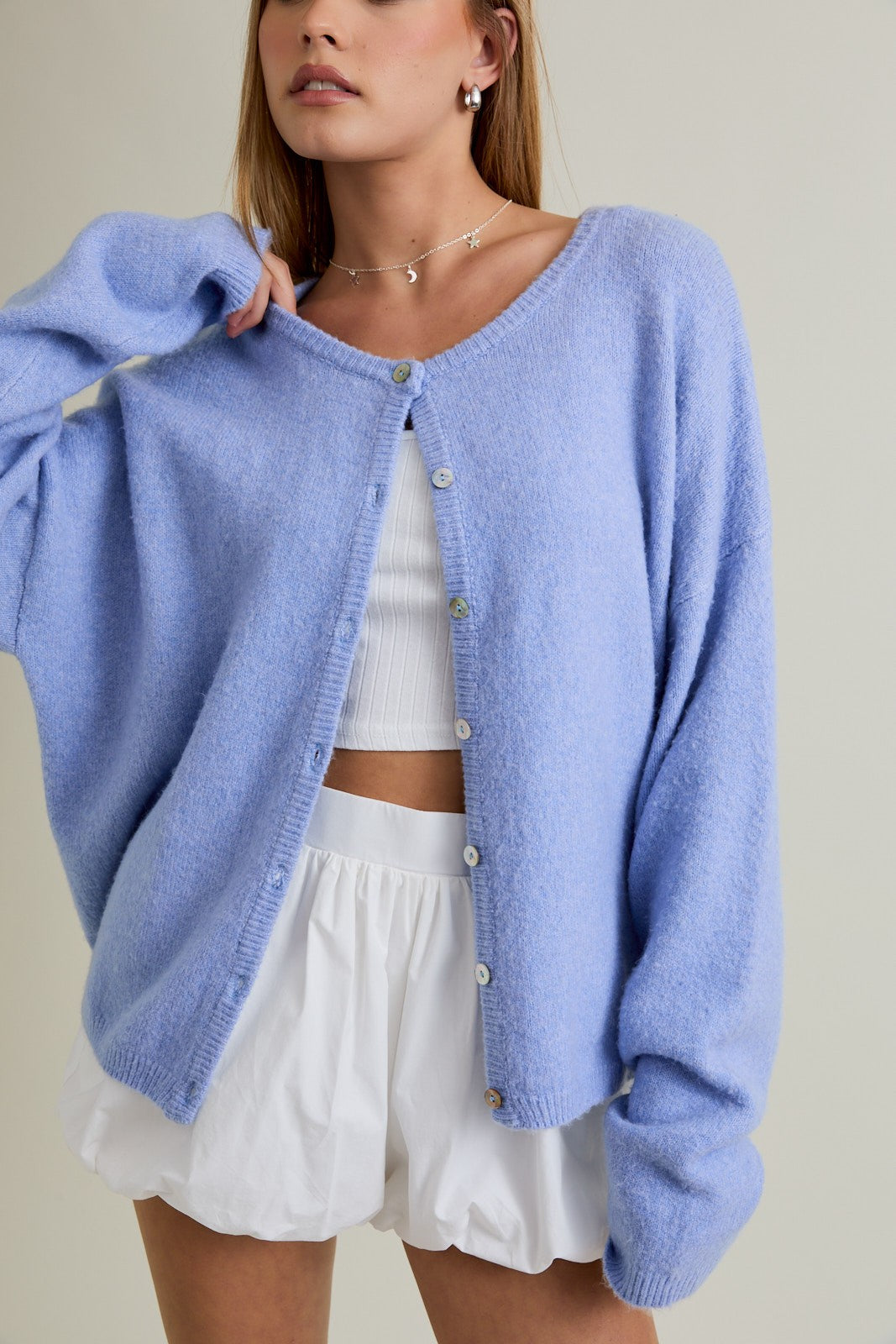 woman wearing a light blue oversized cardigan, buttoned up, over a white crop top and white shorts