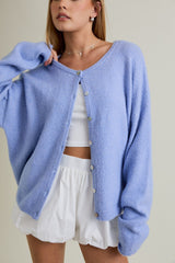 woman wearing a light blue oversized cardigan, buttoned up, over a white crop top and white shorts