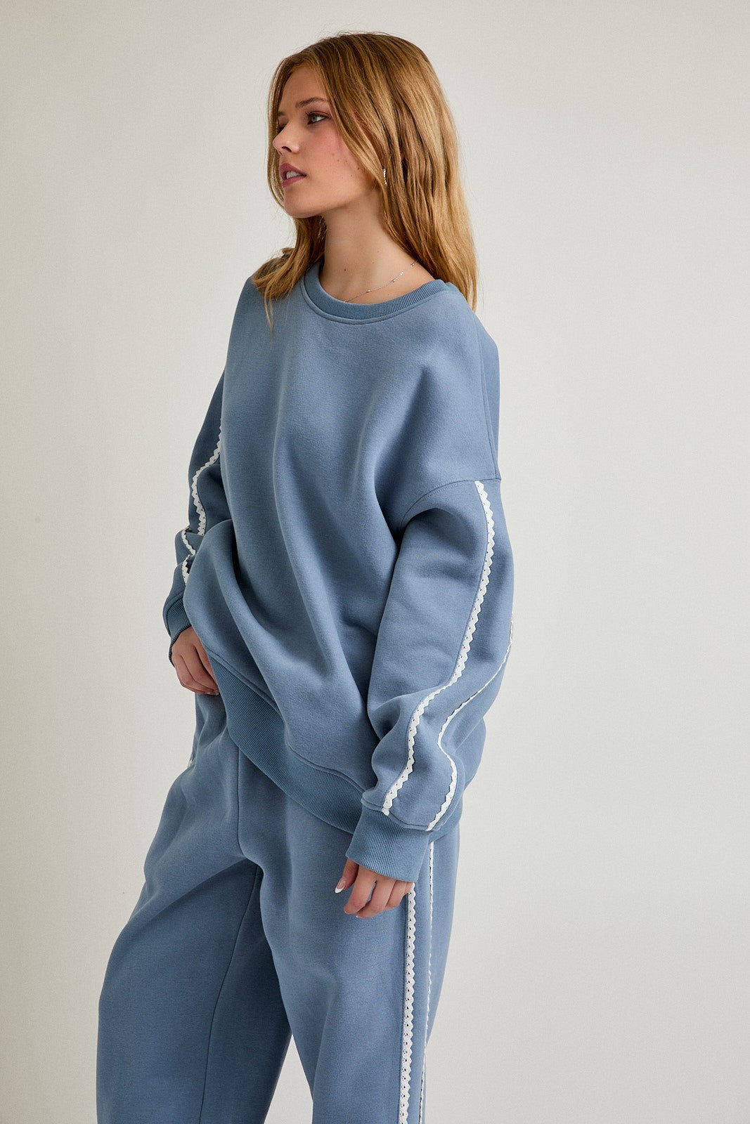 woman wearing a light blue oversized sweatshirt with white side detailing and matching sweatpants
