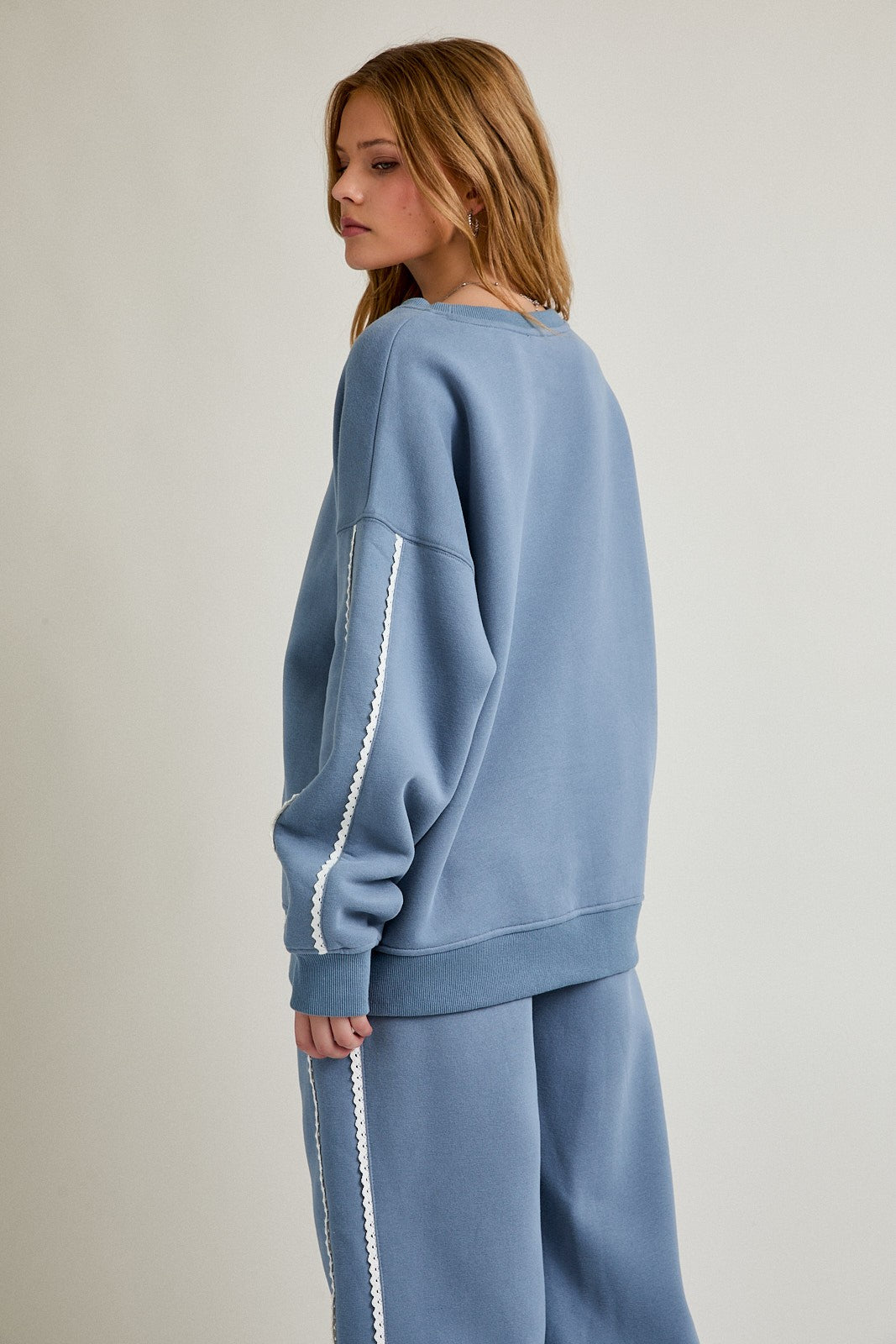 woman wearing a light blue oversized sweatshirt with white trim details and matching sweatpants, seen from the back