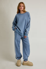 woman wearing a blue sweatshirt and matching joggers with white trim details and tan footwear